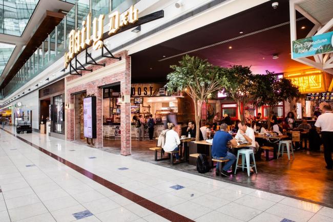 Shop front of The Daily DXB, a foodhall, featuring the logo of the concept and people eating